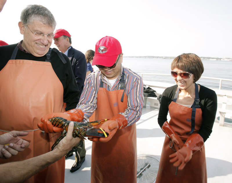 Eliot Cutler, left, laughs as Fang Fenglei holds a lobster Friday aboard the boat Lucky Catch in Portland Harbor. At right is Theresa Gao of COFCO, a Chinese conglomerate and food importer. Members of the group toured Portland Shellfish Co. and had lobster rolls at the Gulf of Maine Research Institute at the invitation of Cutler, an independent gubernatorial candidate.