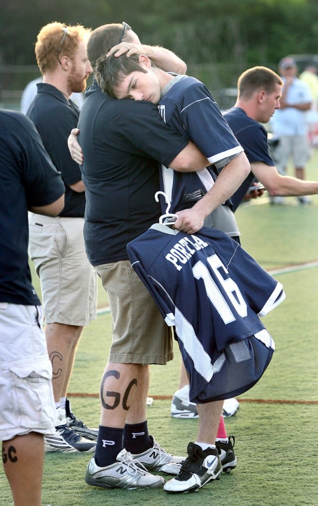 Pat Cormier, whose brother died in a car accident Thursday night, holds his brother's uniform while hugging Portland High assistant coach Josh Graham after the Class A boys' lacrosse state final Saturday.