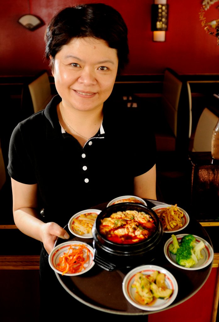 Soju’s owner Catherine Burrill with a soft tofu chigae (spicy tofu stew) surrounded by house kimchees.