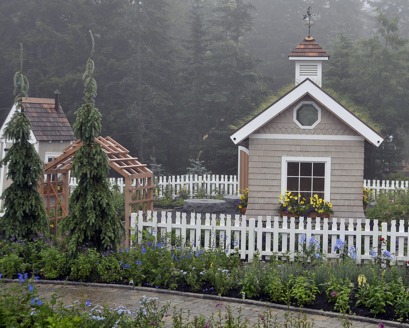A fence with a cat motif surrounds a cottage that sprouts a variety of grasses from the roof. The mission of the garden is education, and it was designed for children to have fun while learning.