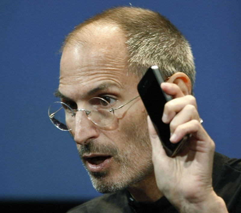 Apple CEO Steve Jobs holds up an iPhone 4 as he talks about how the company plans to address the phone's signal reception problem.