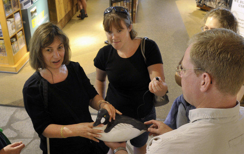 Susan Shapiro, left, of Port Washington, N.Y., one of the volunteers in the interpreting program, is blind and hard of hearing. Student Rachel Morrison holds a small microphone connected to Shapiro’s amplified hearing system so she can understand as Jason Ohman, right, of Bean’s hunting and fishing department, talks about the wooden decoy she is feeling.