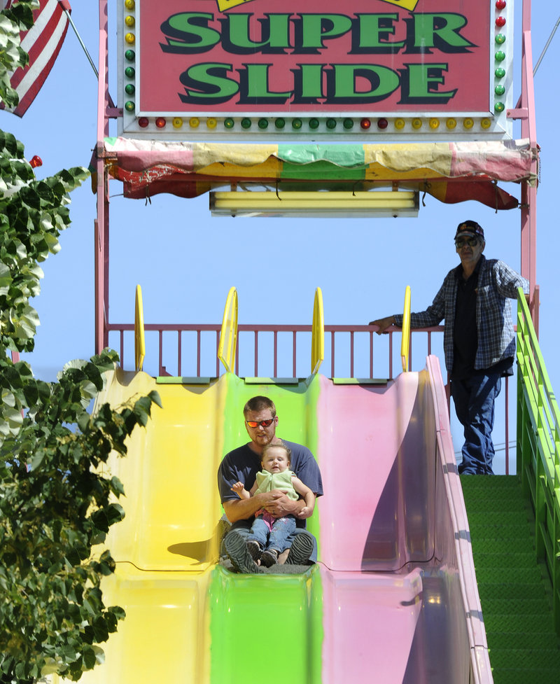 Garret Mathews and his 19-month-old daughter Kayla of Bath try the Super Slide. The festivities culminate in fireworks over the Kennebec River on Monday night.