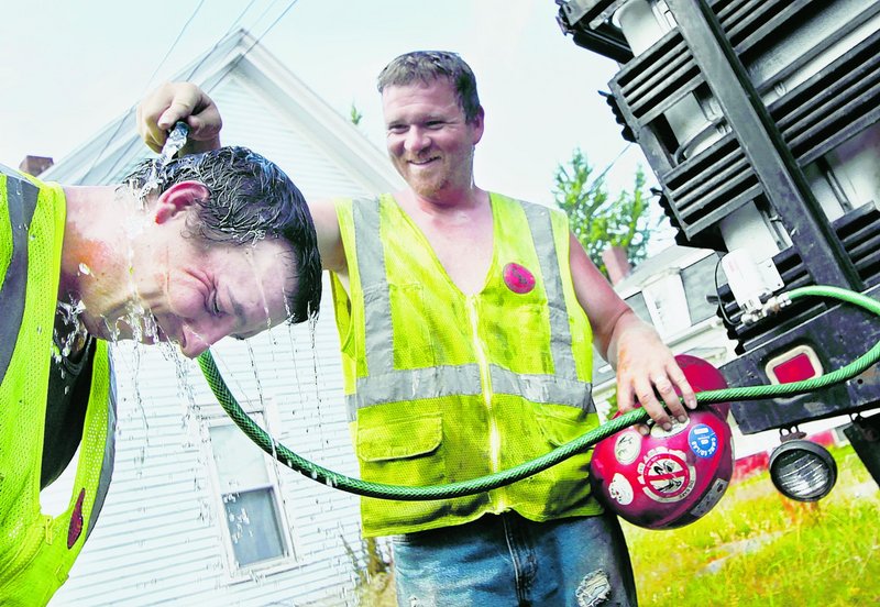 Mike Melanson helps Andrew Eaton cool off during a break with Shaw Brothers Construction in South Portland on Tuesday.