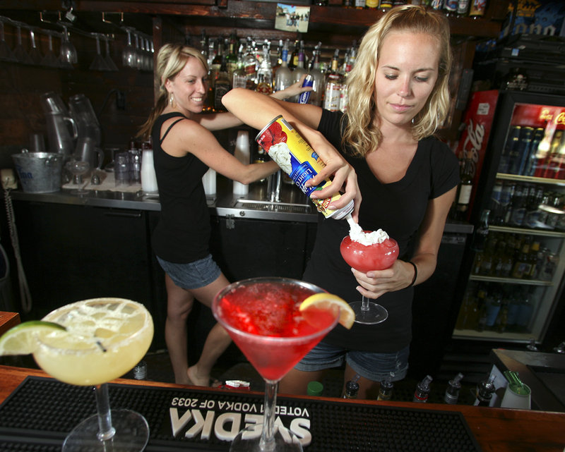 Michelle Merrill applies whipped cream to a strawberry daiquiri as fellow bartender Megan McCullum pours a beer.