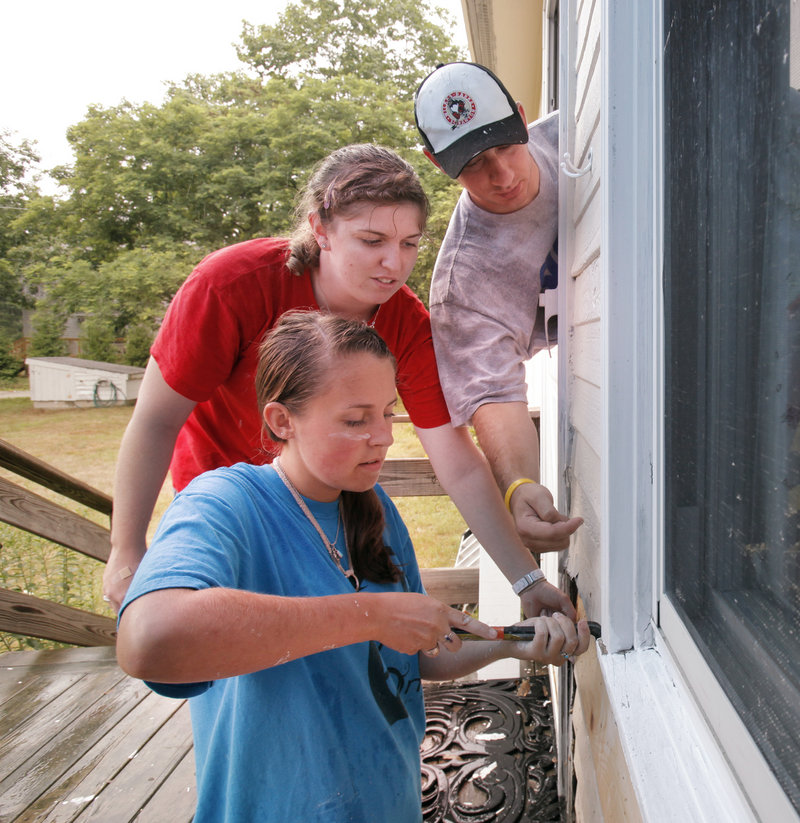 William Tryon, right, offers advice to Hannah Foster, left, and Kallie Hoinacki as the girls install a piece of siding at the Kennebunk home of Cathy McCollet on Wednesday. The three are participating in a program called workcampNE, which puts teenagers to work on home repairs at the houses of elderly and disabled people. Tryon is the crew leader of the group. The camp, which hosts teens from as far away as Illinois and Canada, is using Kennebunk Middle School as its base of operation.