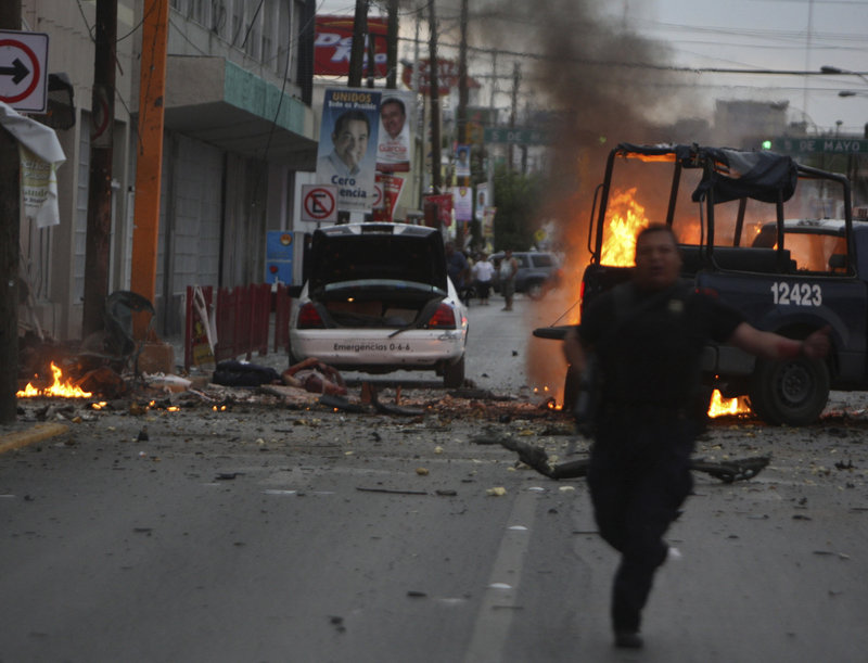 A police officer runs for cover after an attack on police patrol trucks that killed three people in the border city of Ciudad Juarez, Mexico, on Thursday. Mexican investigators ran forensic tests and determined that drug gangs used a car bomb for the first time in the attack.