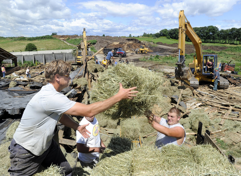 Art McNeally, Jason Mitsin and Nate Faulkner load hay onto a truck Thursday at the Benson dairy farm in Gorham. The three men were among dozens of friends, relatives and neighbors who helped the family clean up after Wednesday's storm.