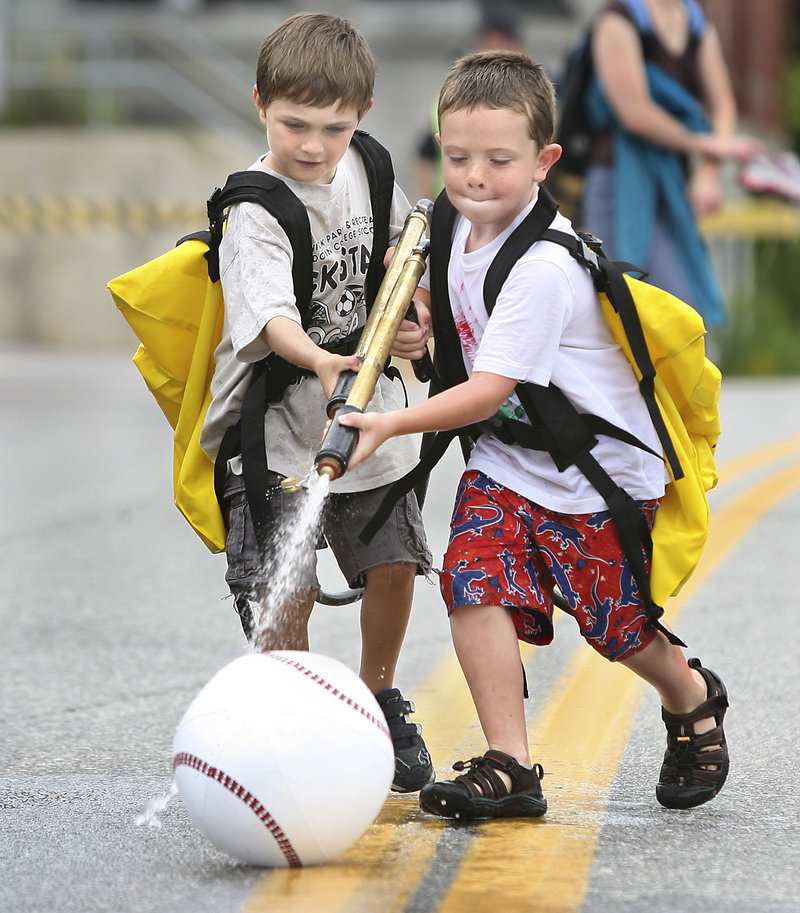 Caden Slater, 5, of Brunswick, left, and Cole Alexander, 6, of Richmond use water backpacks to spray an inflatable ball down the street. The game was sponsored by the Richmond Fire Department.