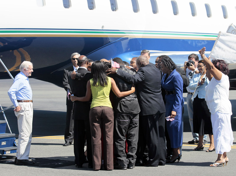 Aijalon Gomes' family huddles around him after his arrival with former President Jimmy Carter, left, at Logan International Airport.