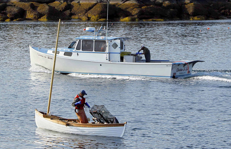 Nat Hussey hauls a trap onto his peapod by hand as a diesel-powered lobsterboat motors by off Matinicus Island.
