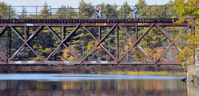 Bicyclists cross a railroad bridge over the Presumpscot River. When converting a rail line to a bike or walking path, it's important not to preclude its return to rail use.