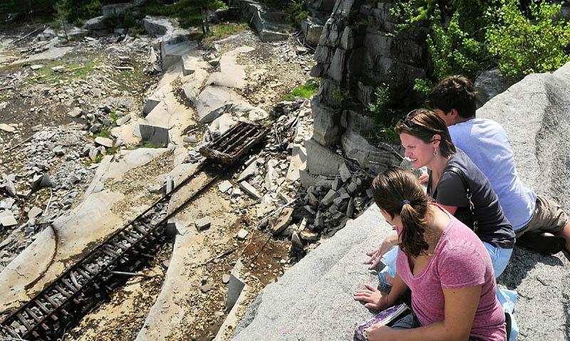 Erin Ballew, left, Cary Colwell and Ethan Ballew sit on the cliffs high above the mostly-drained Stinchfield Quarry looking down at a cart used to move granite during a tour on Sunday afternoon in Hallowell.