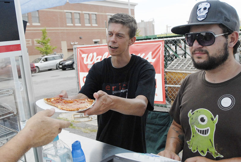 Eric Hughes serves a slice of pizza Tuesday, with his job coach, Logan Abbey, beside him. Each day they roll the food cart a quarter-mile from its storage building to the sales location.