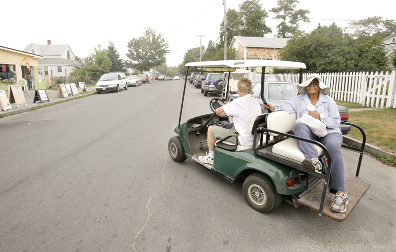 Matt Rand gives a ride to Meikie Jenness on Peaks Island on Aug. 5. Rand said his golf cart is inspected and insured, as required for all golf carts that travel on city roads. But he doesn't have liability insurance for his passengers.