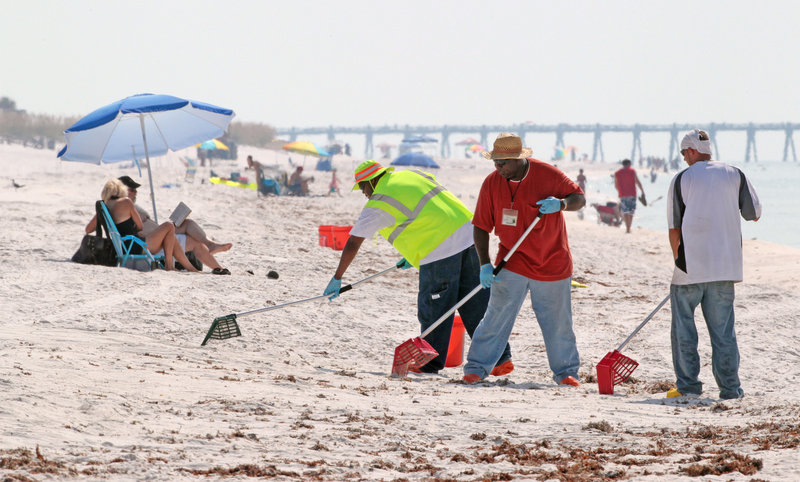 Oil cleanup workers rake for tar balls on Pensacola Beach, Fla., Sunday. Tourism is starting to pick up along the Gulf Coast with the capping of the Deepwater Horizon wellhead.