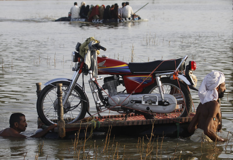 Men push a motorcycle on rubber floats Monday as a police boat passes along a flooded road in Baseera, Punjab province, Pakistan. President Asif Ali Zardari compared anger at the government to the anti-government sentiment generated by the aftermath of Hurricane Katrina in the U.S.