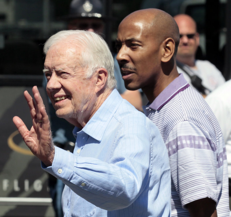 Former President Jimmy Carter waves after arriving at Logan International Airport in Boston with Aijalon Gomes, right, on Friday.