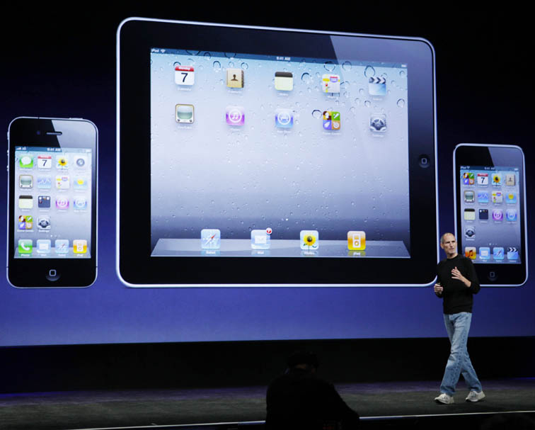 Apple CEO Steve Jobs strolls past a display of the iPhone, left, iPad, and the iPod Touch, right, at news conference in San Francisco today.