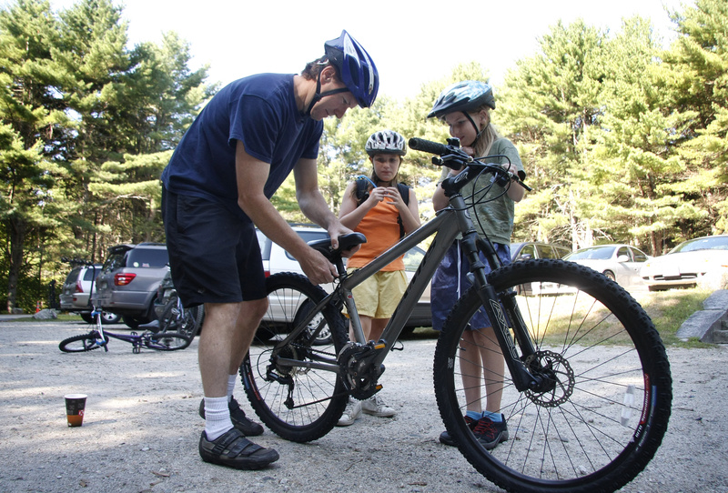 Keith McMullan of South Portland adjusts the seat for his daughter, Lydia, 11, right, as sister Izzy, 9, watches on Saturday before a ride for mountain bike beginners at Bradbury Mountain State Park in Pownal.