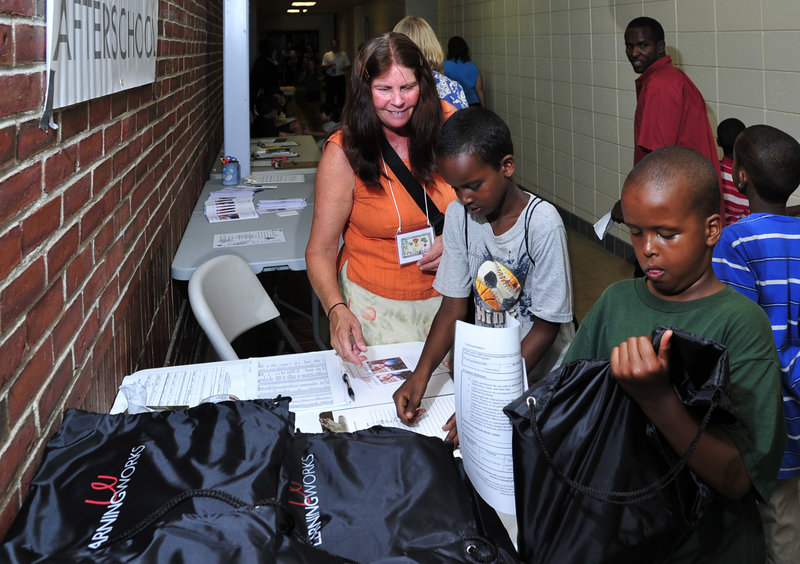 Abdirahim Ali, 9, checks out his new backpack as his friend, Ayub Hiis, 8, signs up Wednesday for his gift, assisted by educational technician Carol Gallagher.