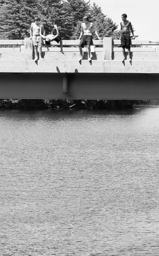 Boys watch as one of their buddies jumps off the bridge that carries Routes 202, 4 and 117 over the Saco River in Buxton last month. Many swimmers still leap from the structure despite warning signs and police efforts to keep them away from the heavily traveled bridge.