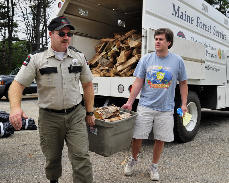 Maine Forest Service Ranger Ritchie Hafford helps John Demoy of Canton, Mass., carry his fresh supply of Maine firewood to his car Friday after exchanging the out-of-state firewood Demoy brought from Massachusetts.