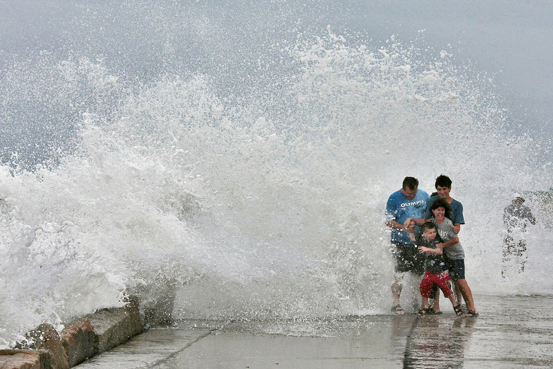 The Gallishaw family from Seekonk, Mass., braces for a large wave crashing over the Goosebury Island causeway in Westport, Mass., on Friday. People were warned to stay off beaches because of the danger of getting swept away.