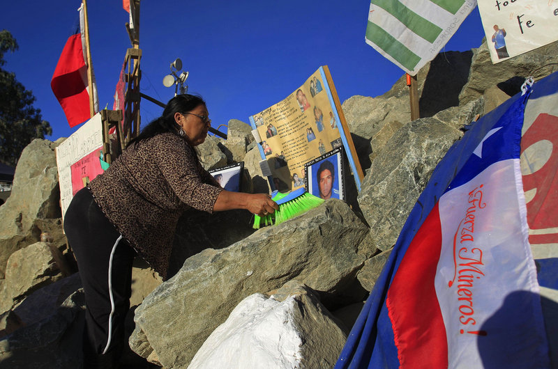 Maria Gomez, an aunt of trapped miner Jimmy Sanchez, cleans his photos on display Tuesday outside the mine where 33 are trapped in Copiapo, Chile.