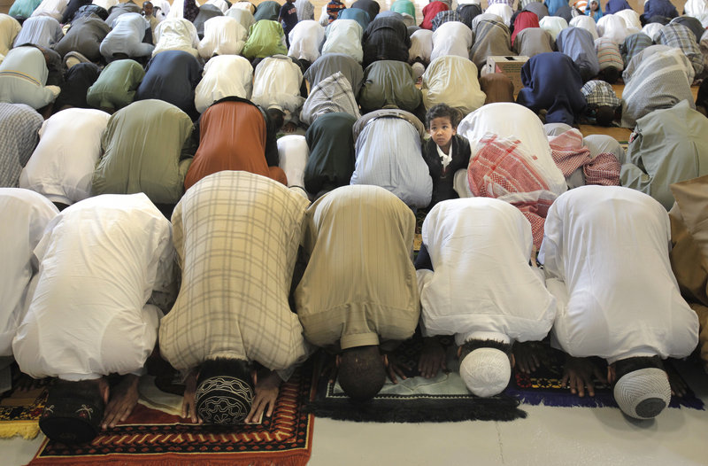 A boy looks up while men bow in prayer during the Eid al Fitr celebration at the Portland Expo on Friday. Eid al Fitr marks the end of Ramadan, the Islamic holy month when Muslims fast from dawn to sunset. Women prayed on the other side of the hall.