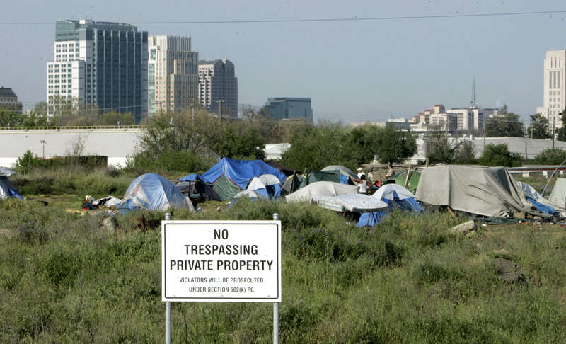A camp for homeless people rises behind a “No Trespassing” sign in Sacramento, Calif. Analysts estimate that 45 million Americans, or more than one in seven, were poor last year.