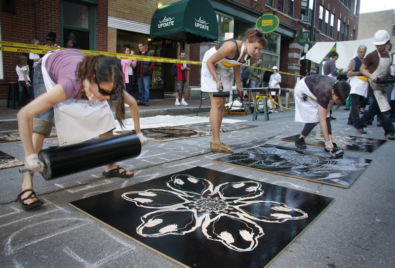 Carrie Scanga of Brunswick, left, and Irina Skornyakova of Portland, center, roll ink onto giant woodblocks created by local artists during the Space Gallery Block Party on Congress Street in Portland on Saturday. The woodblocks were then printed on bed-sheet-sized pieces of canvas with a giant steamroller provided by Pickwick Independent Press.