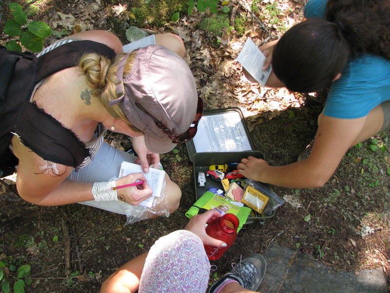 Shannon Bryan records her find in a logbook as her geocaching friends look through the cache contents.