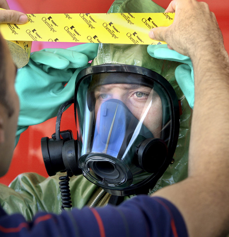 Police officer Dan Townsend places a piece of tape on the hazardous material suit of firefighter Phil LaRou, as LaRou prepares to contain a spill during Thursday’s Weapons of Mass Destruction team exercise on Read Street.