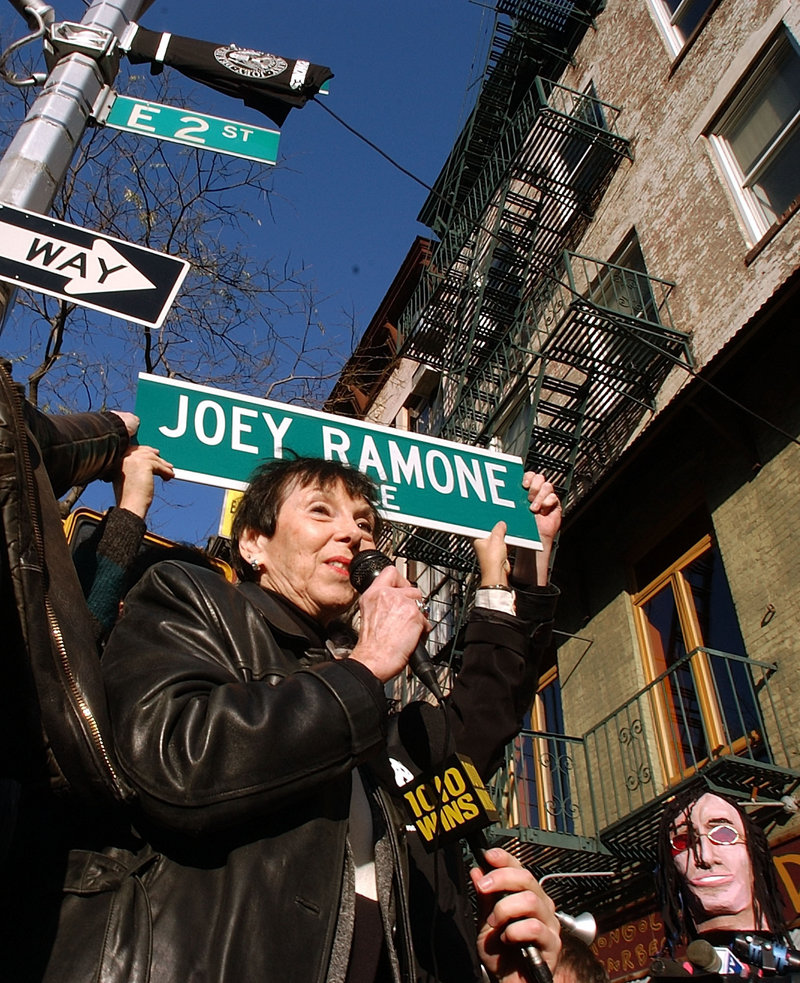 In this 2003 file photo, Charlotte Lesher, the mother of late singer Joey Ramone, holds a sign that names the corner of Bowery and 2nd Street in New York as Joey Ramone Place.