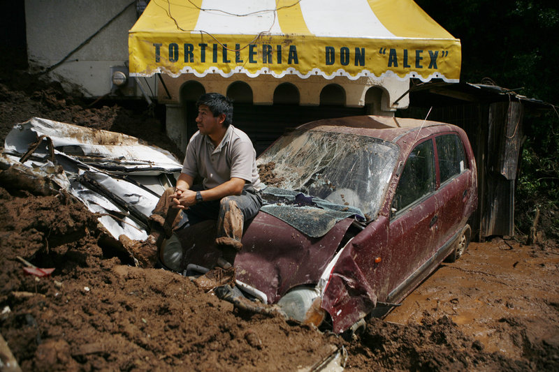 A man rests on a damaged vehicle Wednesday in the aftermath of a landslide in Santa Maria de Tlahuitoltepec in Oaxaca state, Mexico. The government delivered blankets and other supplies to survivors and others who fled their unstable homes for fear of more mudslides.