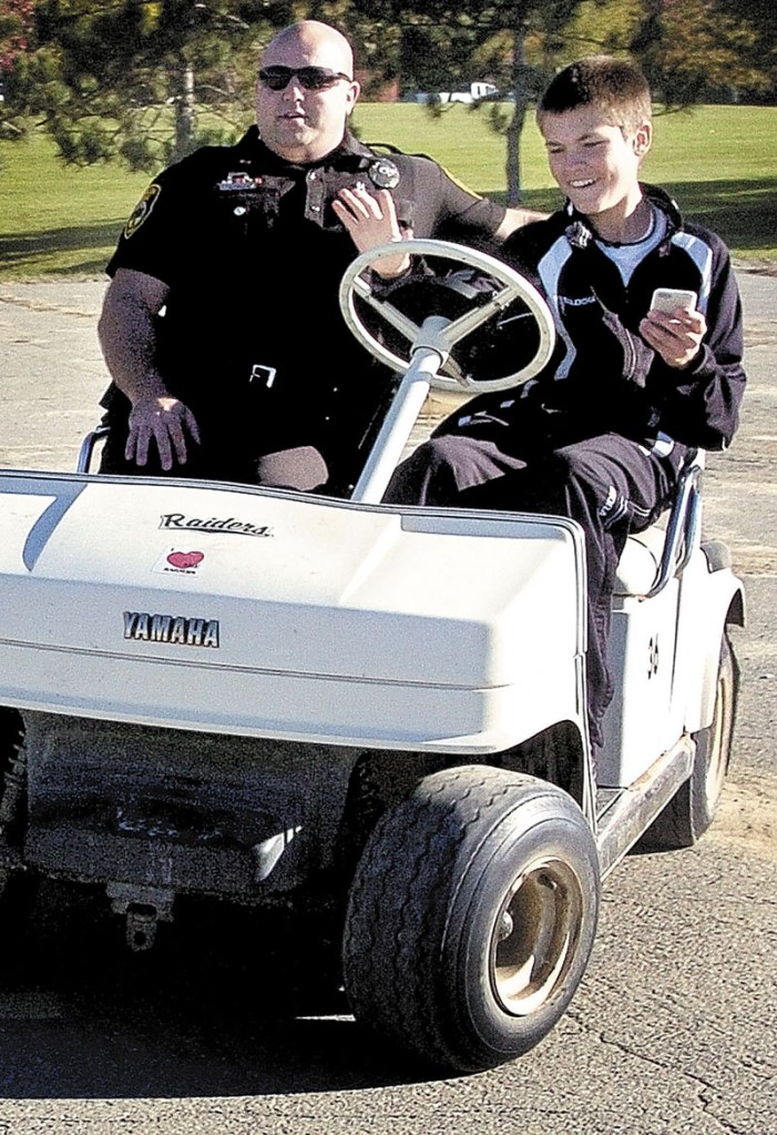 Logan Vashon, a 14-year-old freshman at Winslow High School, attempts to drive a golf cart while texting on a cell phone Wednesday morning in a parking lot near the elementary school. Sitting beside Vashon is Winslow police officer Joshua Veilleux, who discussed with students the dangers of texting while driving.
