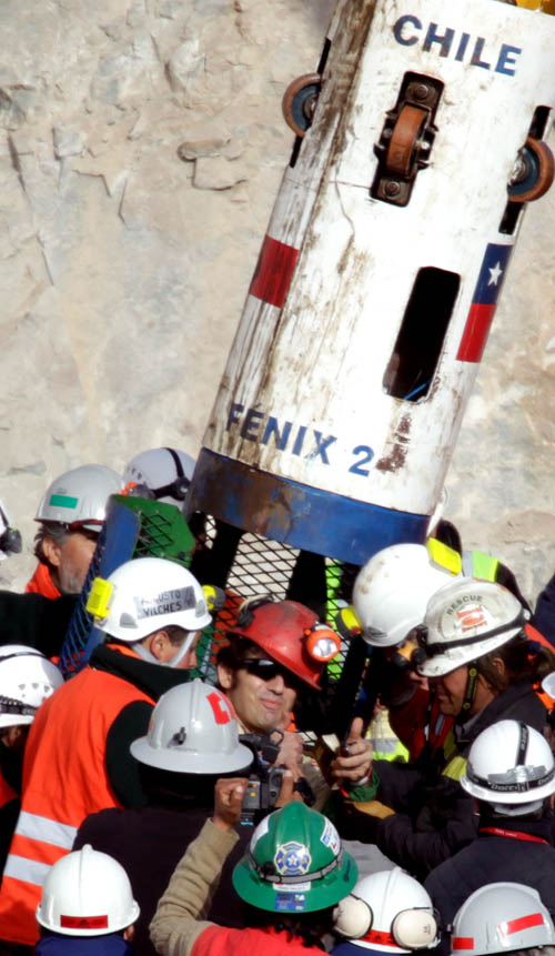 Miner Alex Vega Salazar, center, gives a thumbs up after emerging from the capsule that brought him to the surface today from the collapsed San Jose gold and copper mine.