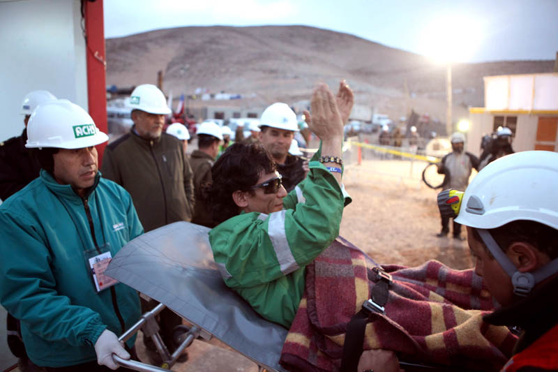 In this photo released by the Chilean government, miner Claudio Yanez applauds as he is carried away in a stretcher after being rescued early today.