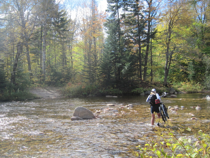 Kate Hossler carries her bike across the shallow but cold Swift River to reach the trail on the other side.