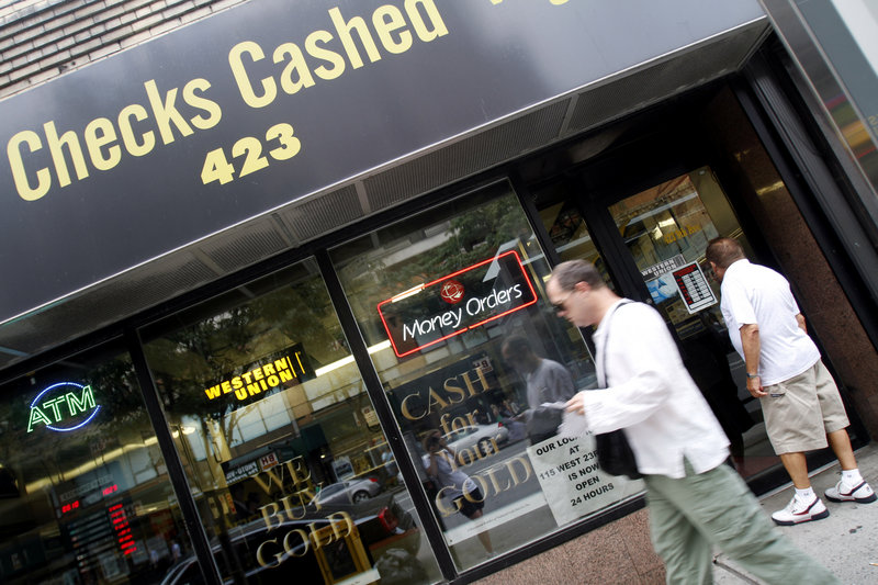 A man looks into the UBNY check-cashing store as another walks past, in the Hell’s Kitchen neighborhood of Manhattan in New York last August. A federal study last year found that about one in four U.S. households skirts banks and relies on services such as check-cashing and payday loans.