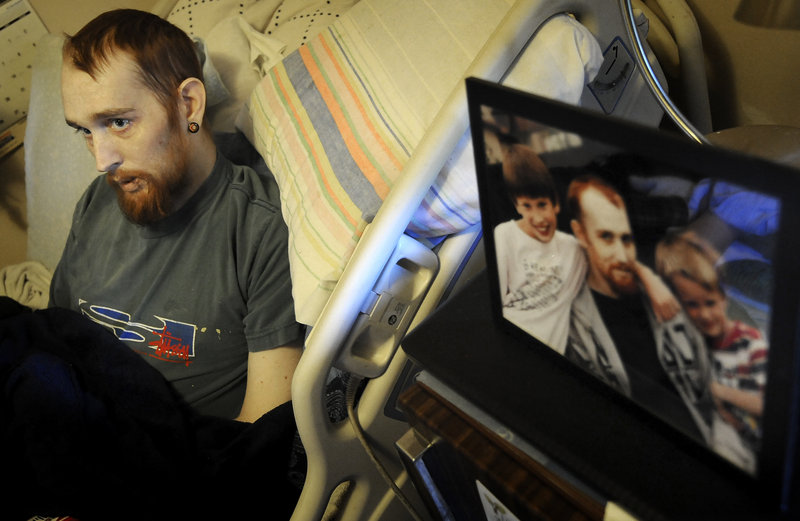 Anthony Napoleone, at home in Salina, Kan., on Thursday, lies next to a picture of him with his sons, Parish, left, and Gage, who live in Maine and visited him recently in Kansas. Napoleone’s family is trying to raise the money to bring the dying man to Maine to be with his children.