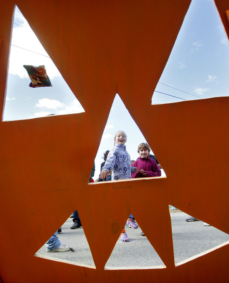 Lucy Valenti, 9, of Cambridge, Mass., tosses a bag through the eye of a pumpkin cut-out as her friend Anya Cunningham, 8, watches on Saturday during Damariscotta's Pumpkinfest.