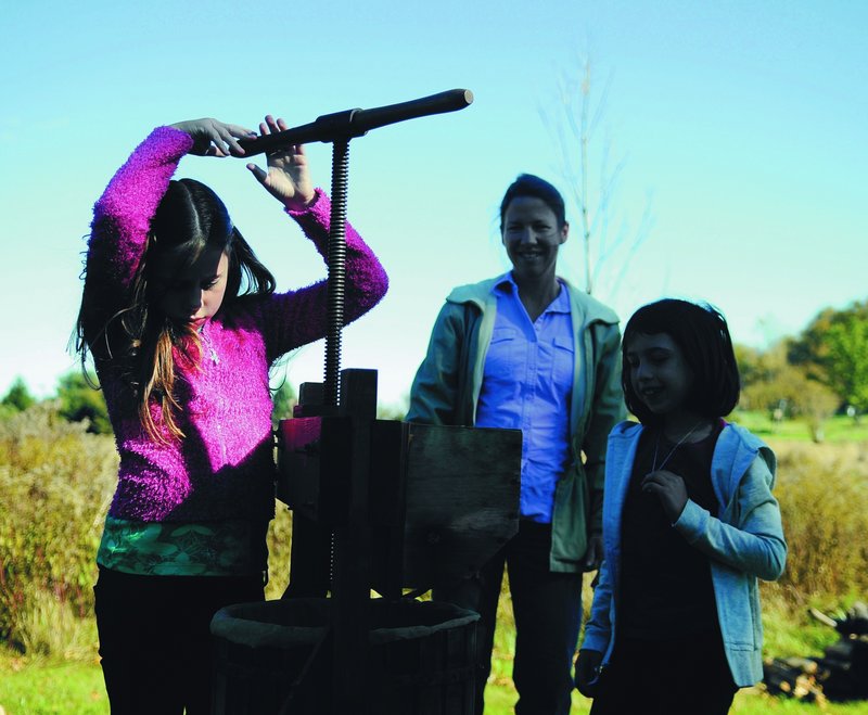 Geneva Smith, 9, turns the apple press Monday at the Viles Arboretum in Augusta, as she learns to make cider with her mother, Jodi, and sister, Leah, 7.