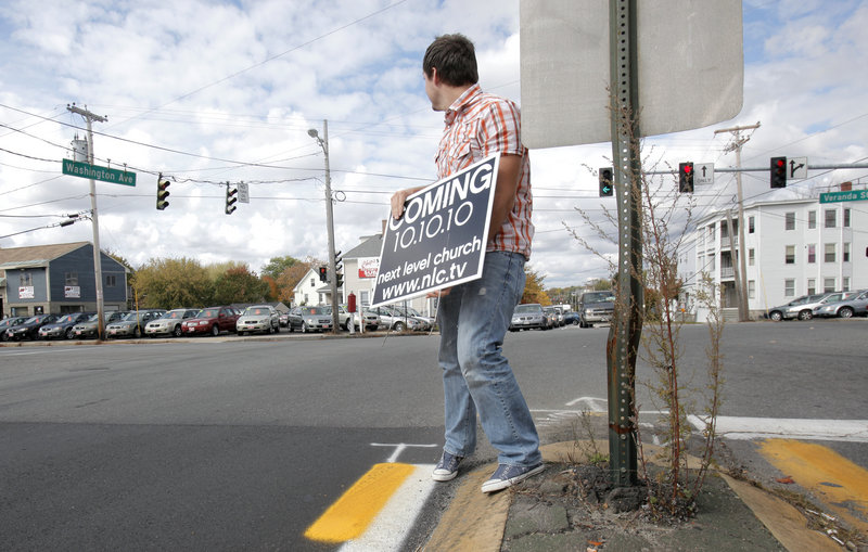 Allen Robbins, the local pastor of the Next Level Church, removes a sign announcing the opening of the church from the median of Washington Avenue in Portland on Thursday.