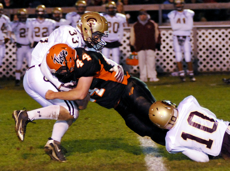 Nick Gagne of Biddeford stretches for extra yards Friday night while being brought down by Josh Remmes, left, and Nate Colpitts of Thornton Academy during their rivalry game at Waterhouse Field. Biddeford won 27-22, beating the Golden Trojans for the first time in five years.