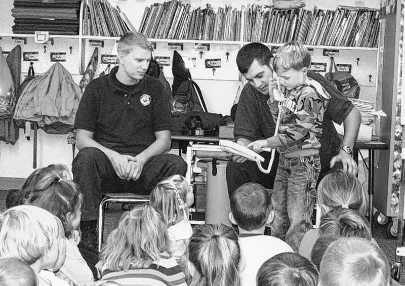Standish firefighters Will Flanders, left, and Adam Royer show kindergarten student Darren Haskell how to call 911 during a recent fire safety event at Edna Libby Elementary School in Standish.