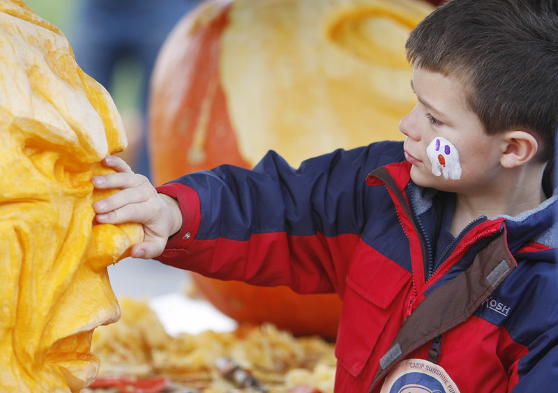 Noah Badeau, 7, of Gorham feels the nose of a 200-pound pumpkin head carved by Moe Auger of Alfred, at Camp Sunshine's annual Pumpkin Festival in Freeport on Saturday.