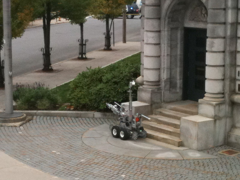 A police robot is maneuvered into position to examine a suspicious package found near the entrance of the federal courthouse in Portland today.
