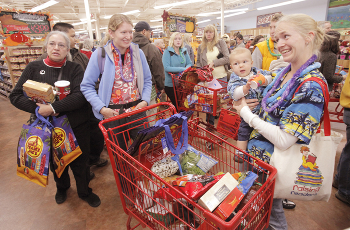 Clad in Hawaiian shirts, Emily Hickey of Gorham, right, holds her son Clayton, 10 months, and talks with her friend Liz Hornor while waiting in the checkout line at Trader Joe's in Portland. The long-awaited store opened this morning and drew a large crowd of shoppers.